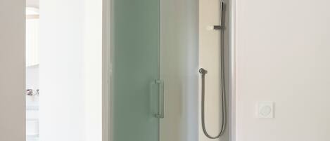 A narrow doorway leading to a shower area with a handheld showerhead and a wall-mounted faucet.