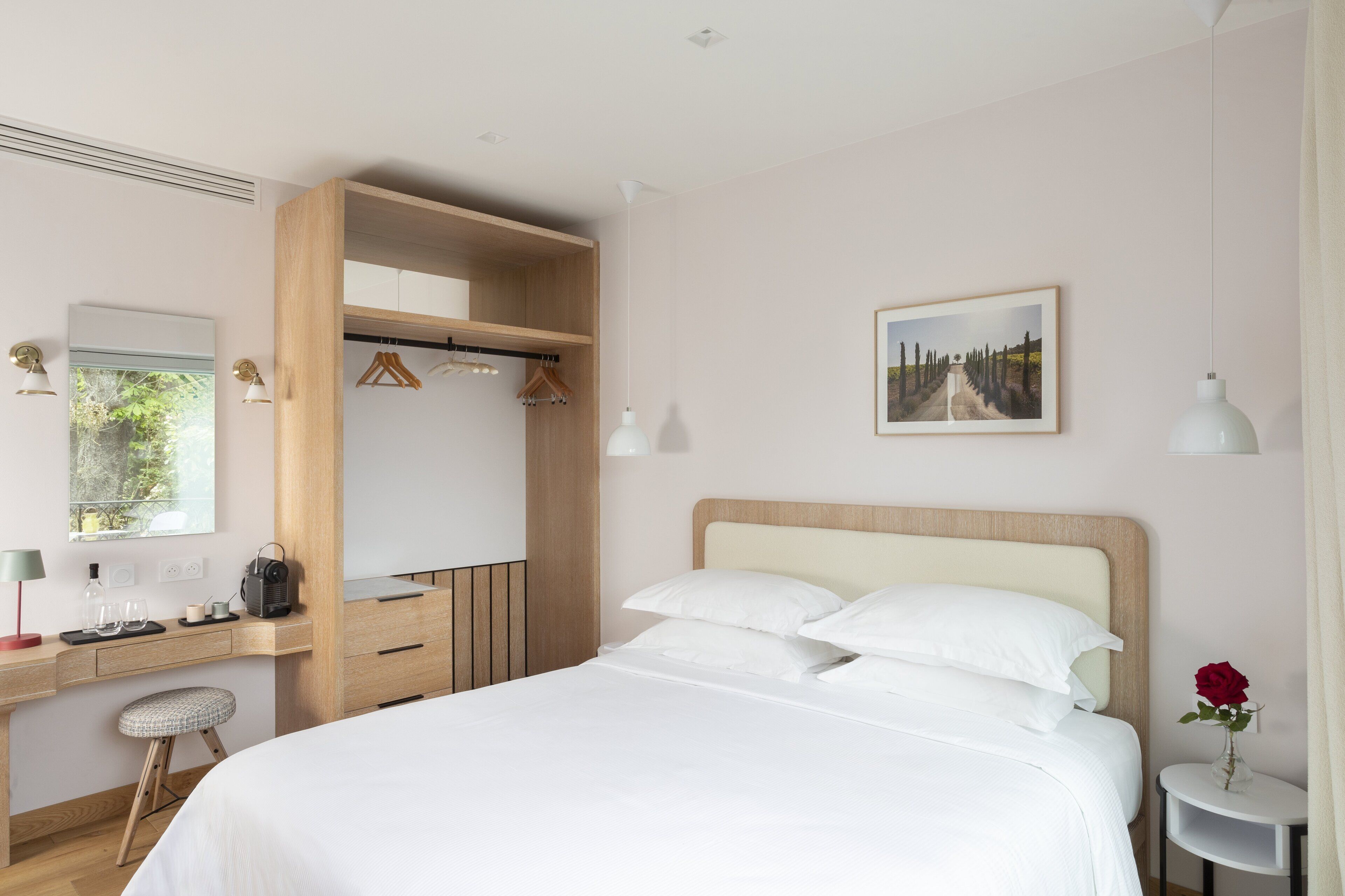 Una camera d'albergo con un letto, una scrivania con un computer, una sedia, un armadio e un comodino con un vaso di fiori.