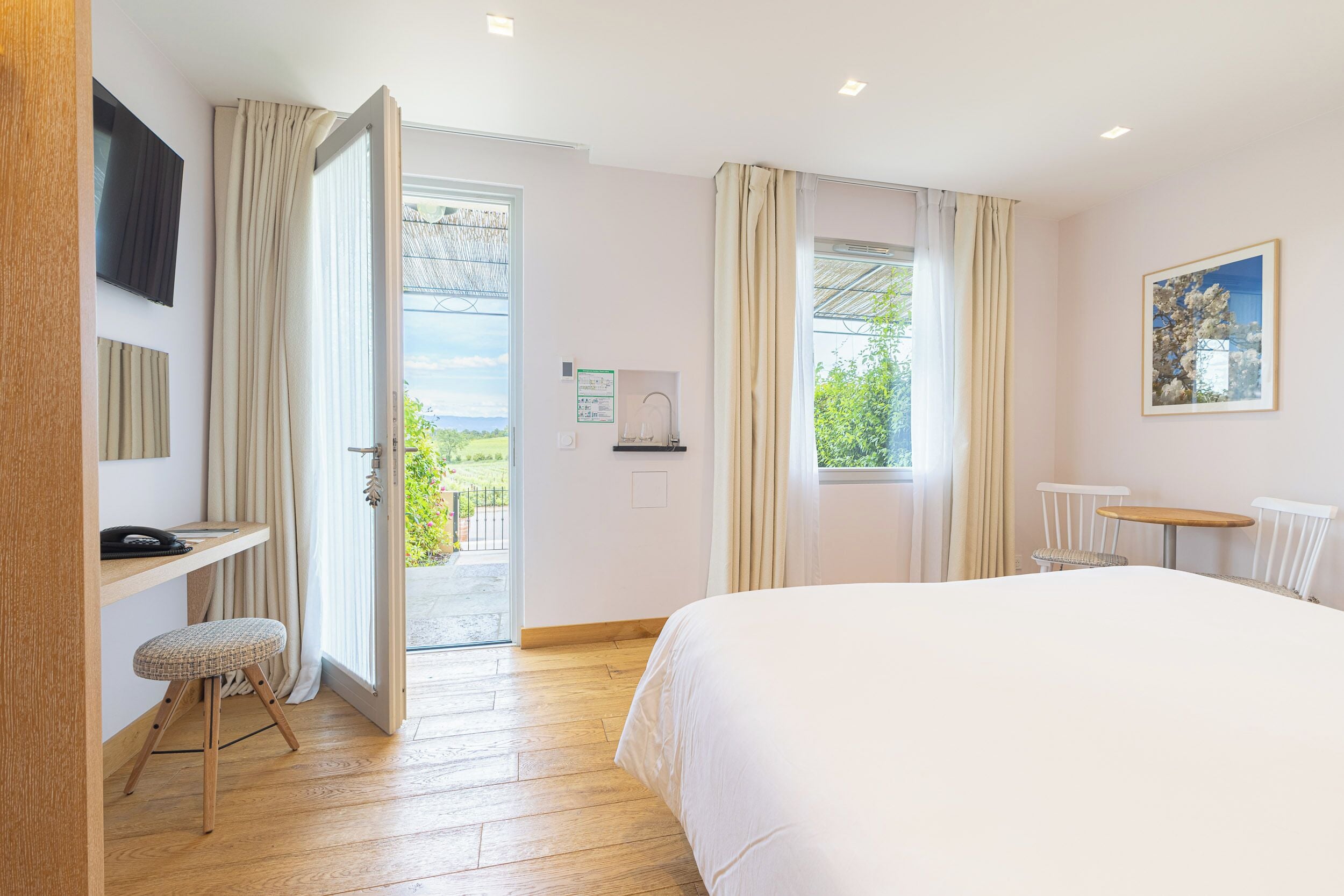 A bedroom with a bed, a desk, a chair, a small table, and a window with curtains.