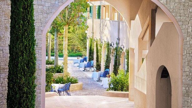 An outdoor dining area with tables and chairs, surrounded by stone walls and greenery. - Auberge La Coste (Le Puy-Sainte-Reparade)