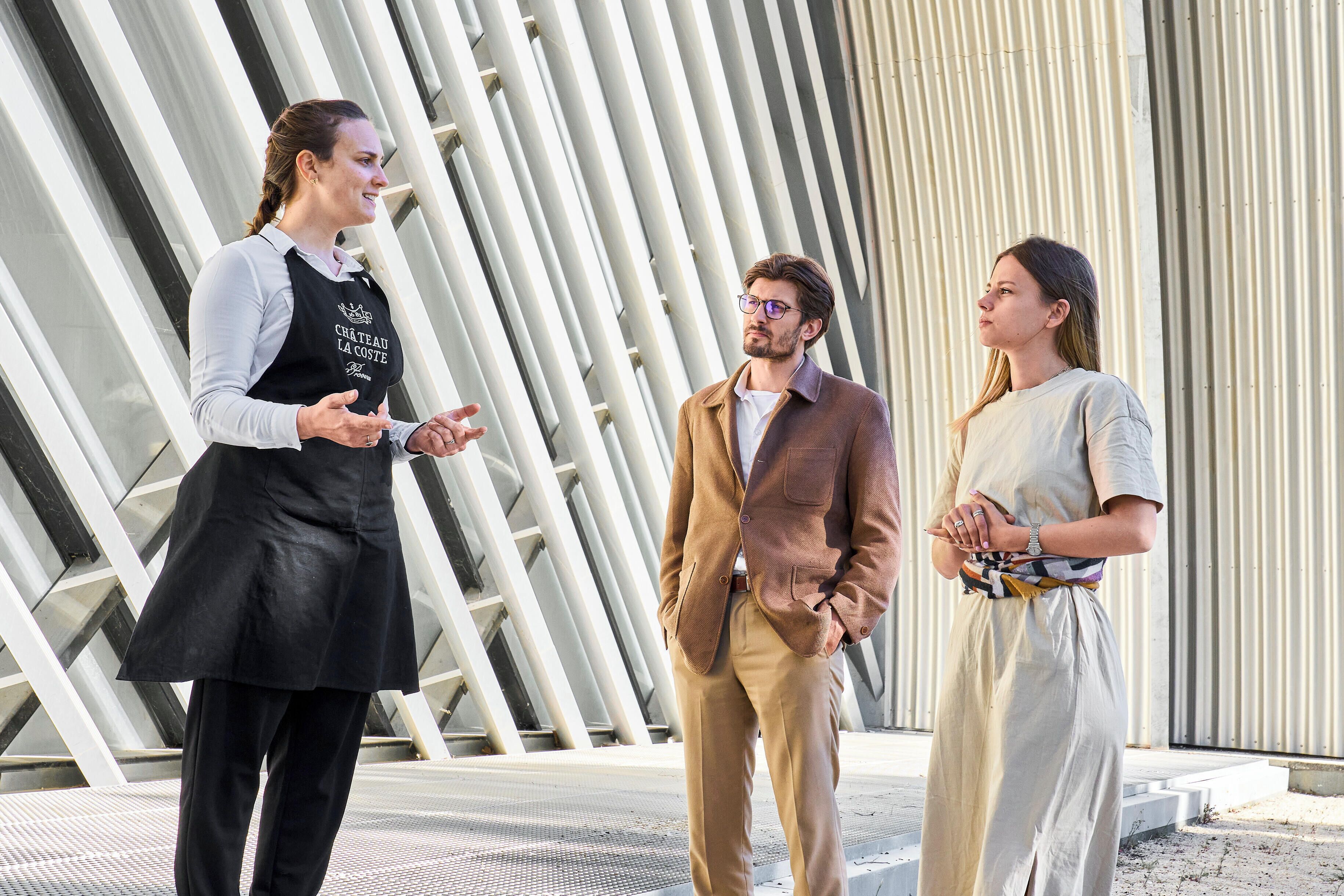 Three people standing in front of a modern architectural structure with vertical lines.