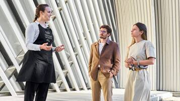 Three people standing in front of a modern architectural structure with vertical lines.