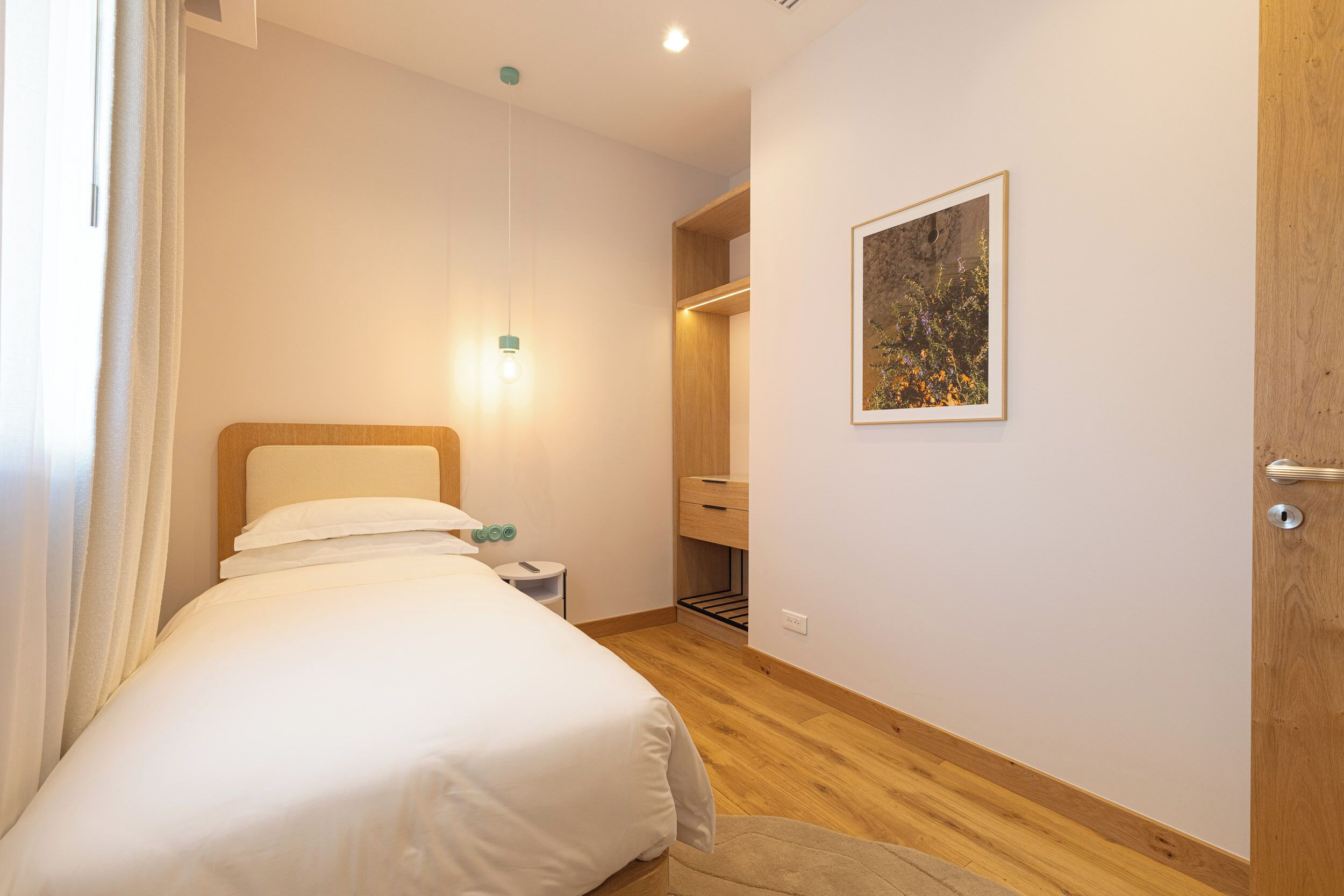 A bedroom with a bed, bedside table, lamp, and a framed picture on the wall.