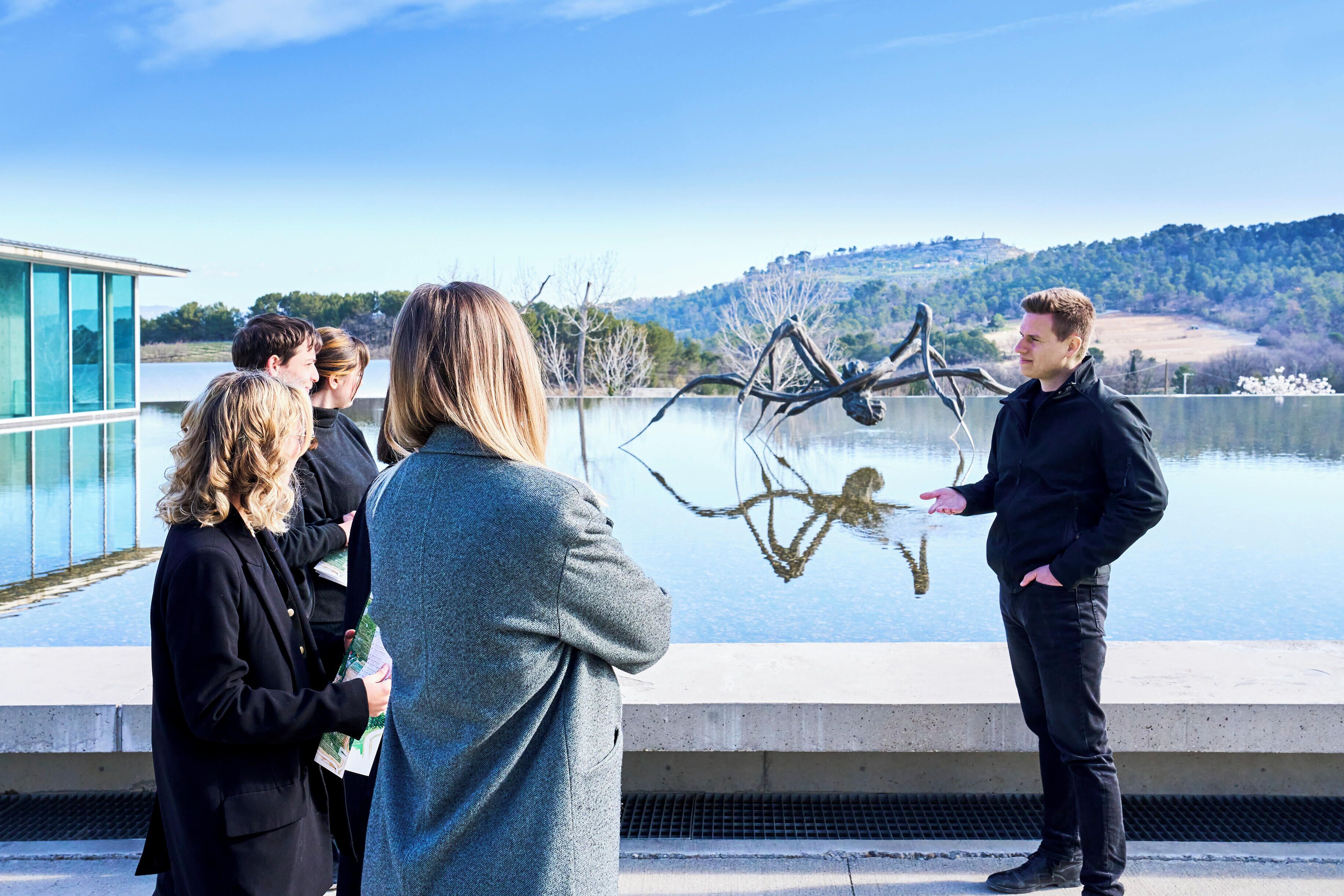 A group of people standing by a body of water with a modern building in the background.