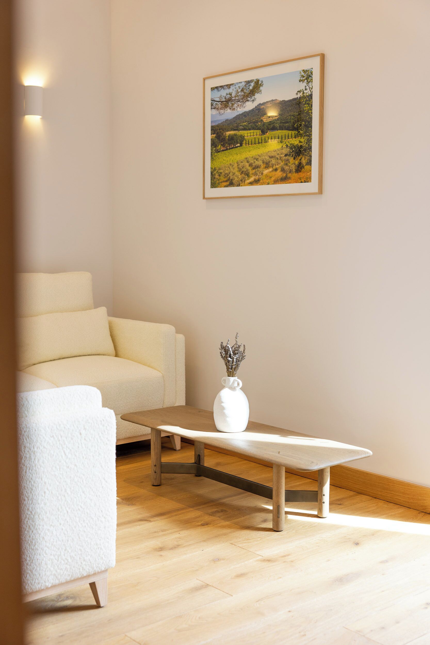 Une pièce avec un canapé blanc, une table basse en bois et un tableau représentant un paysage, accroché au mur.