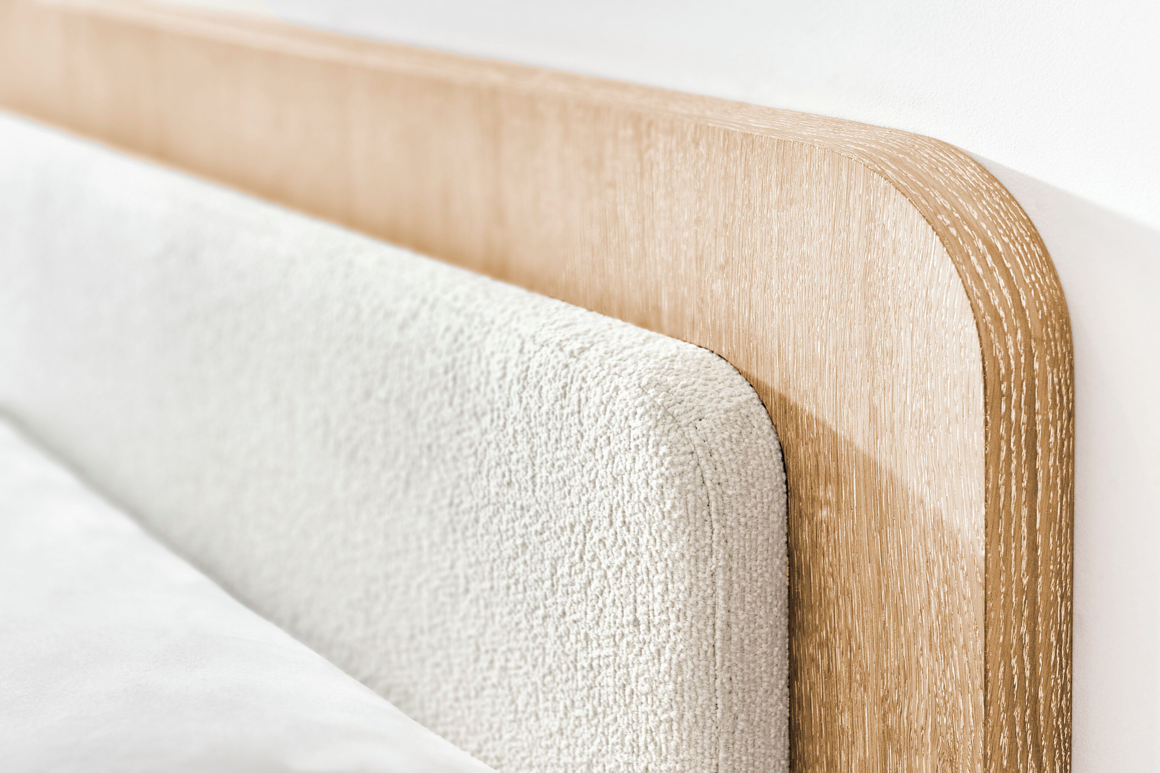Primer plano de una cama con cabecera de madera y colchón blanco con textura.
