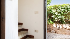 Una escalera con escalones de madera que conduce a un suelo de baldosas de piedra, un aplique de pared y un tapiz tejido.
