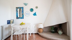Un comedor con una mesa blanca, sillas, un cuenco de fruta y platos decorativos en la pared.
