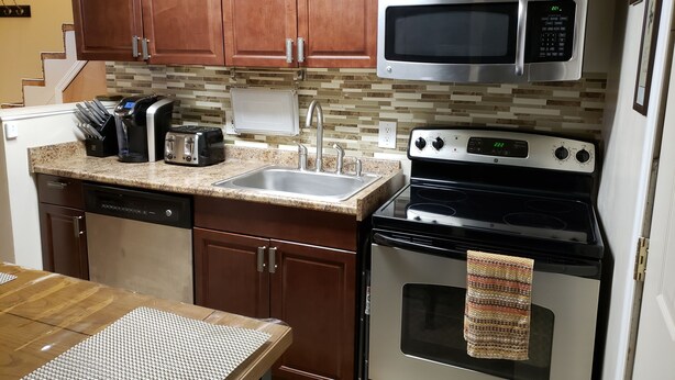 A compact kitchen with wooden cabinets, a stainless steel microwave, a built-in oven, a dishwasher, and a granite countertop. - 1-bedroom apartment in Albany with WiFi, AC (Menands)