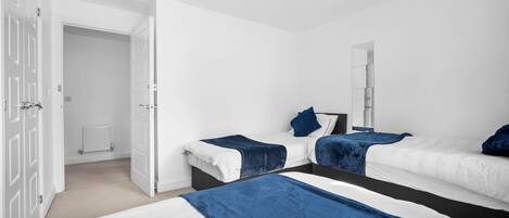 A modern bedroom with two beds, a large mirror, and a door leading to another room.