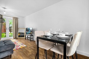 A dining area with a black table set for four, white chairs, and a television in the background.