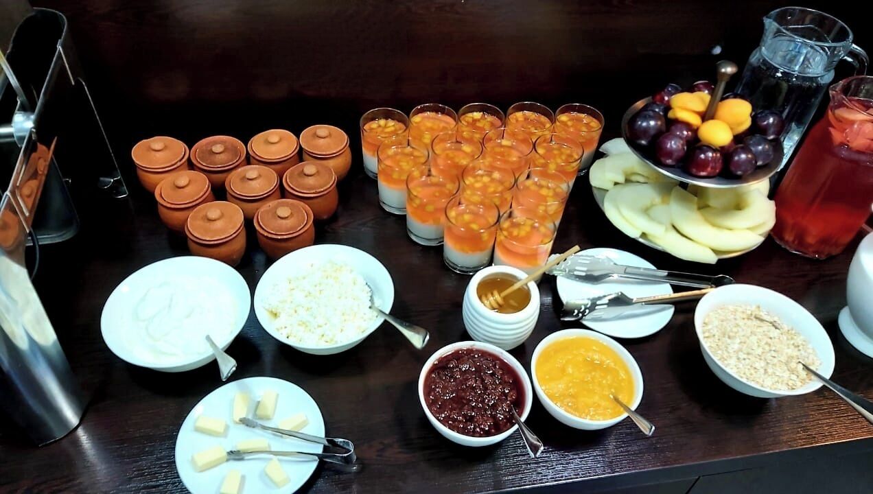 Een buffettafel met diverse etenswaren en drankjes, waaronder fruit, salades en verschillende soorten sauzen.
