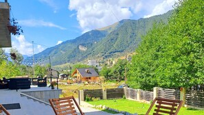 A patio with wooden lounge chairs and a table with a flower arrangement, overlooking a mountainous landscape. - Hotel Mountain Mestia (Mestia)
