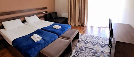 Habitación de hotel con cama, dos mesitas de noche, un escritorio, una silla, televisor y una alfombra estampada.