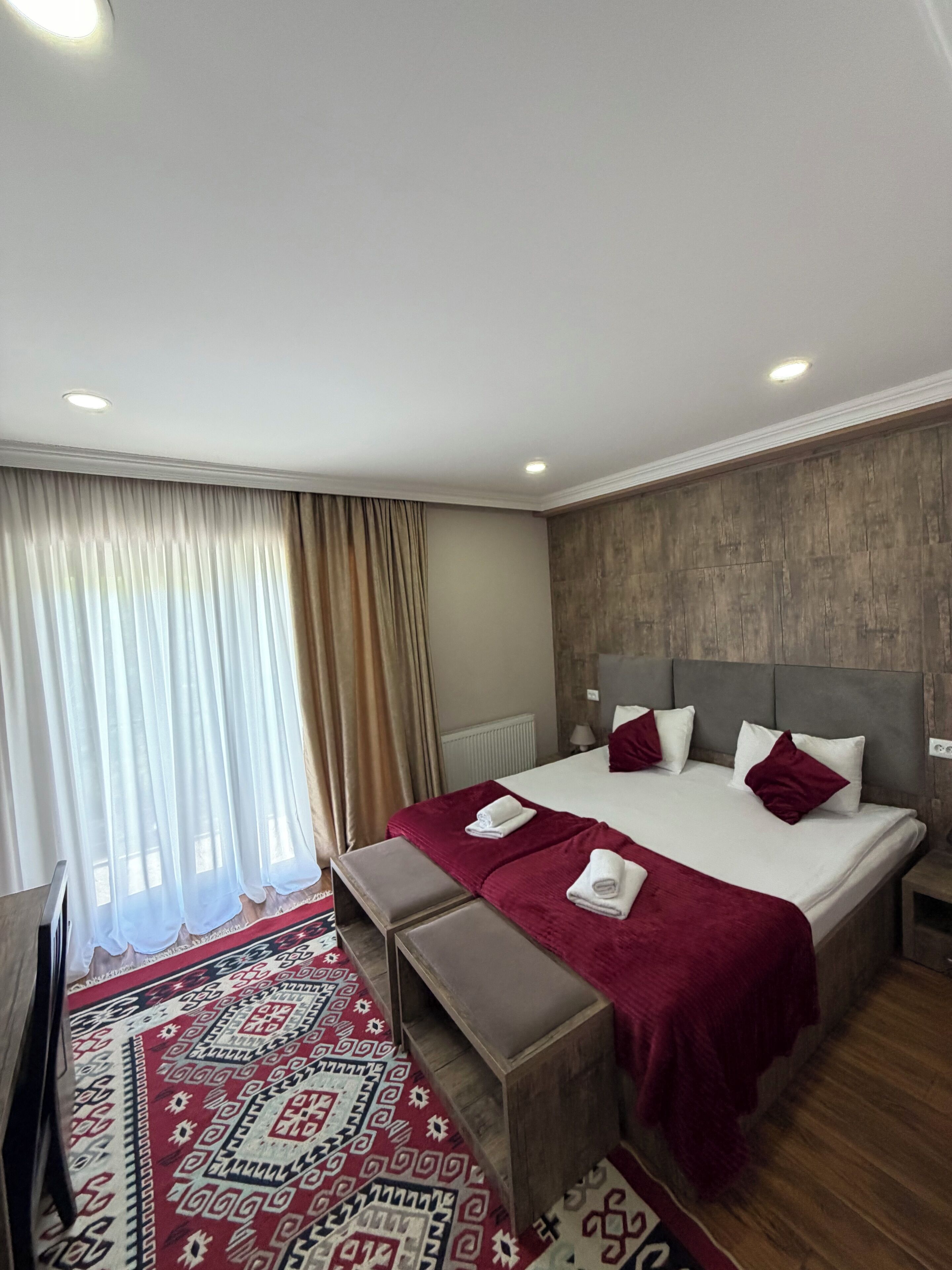 A hotel room with a large bed, a bench, a TV, a patterned rug, and a wooden headboard.