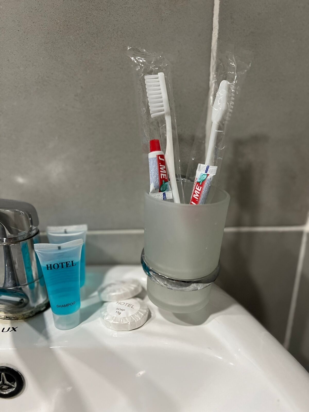Uma pia de banheiro com um porta-escovas de dentes contendo duas escovas e tubos de creme dental.
