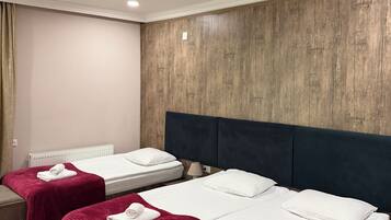 Habitación de hotel con dos camas, cada una con una manta roja y almohadas blancas, un cabecero de madera y una mesita de noche pequeña.