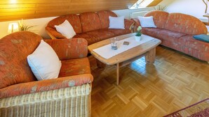 A cozy living room with a large wicker sofa, a wooden coffee table, and a patterned rug.