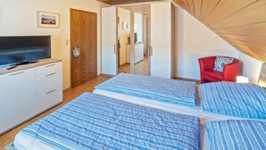 A bedroom with two beds, a TV, a wooden door, and a red chair.