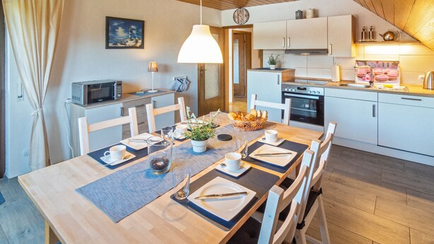 A modern kitchen with white cabinets, a microwave, and a stove. There is a dining table set with plates, cutlery, and a basket of bread.