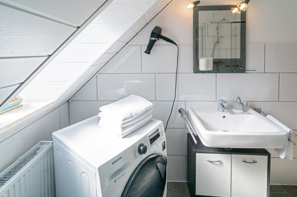 A compact hotel bathroom with a washing machine, a sink, and a mirror.