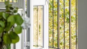 A window with a view of a garden, a metal railing, and a door with a key lock. - Lux Regents Park 2 bed 2 Bath Flat With AC (London)