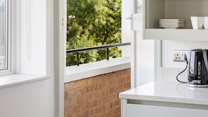 A modern kitchen with white cabinetry, a window with a view of trees, and a kettle on the counter. - Lux Regents Park 2 bed 2 Bath Flat With AC (London)
