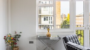 A modern living room with a glass table, a black leather chair, and a potted plant. - Lux Regents Park 2 bed 2 Bath Flat With AC (London)