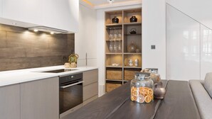 Une cuisine moderne dotée d’un four encastré, d’un plan de travail blanc et d’un pare-feu en bois. On y trouve également un coin repas avec une table en bois foncé et un bocal en verre rempli de tranches d’orange séchées.