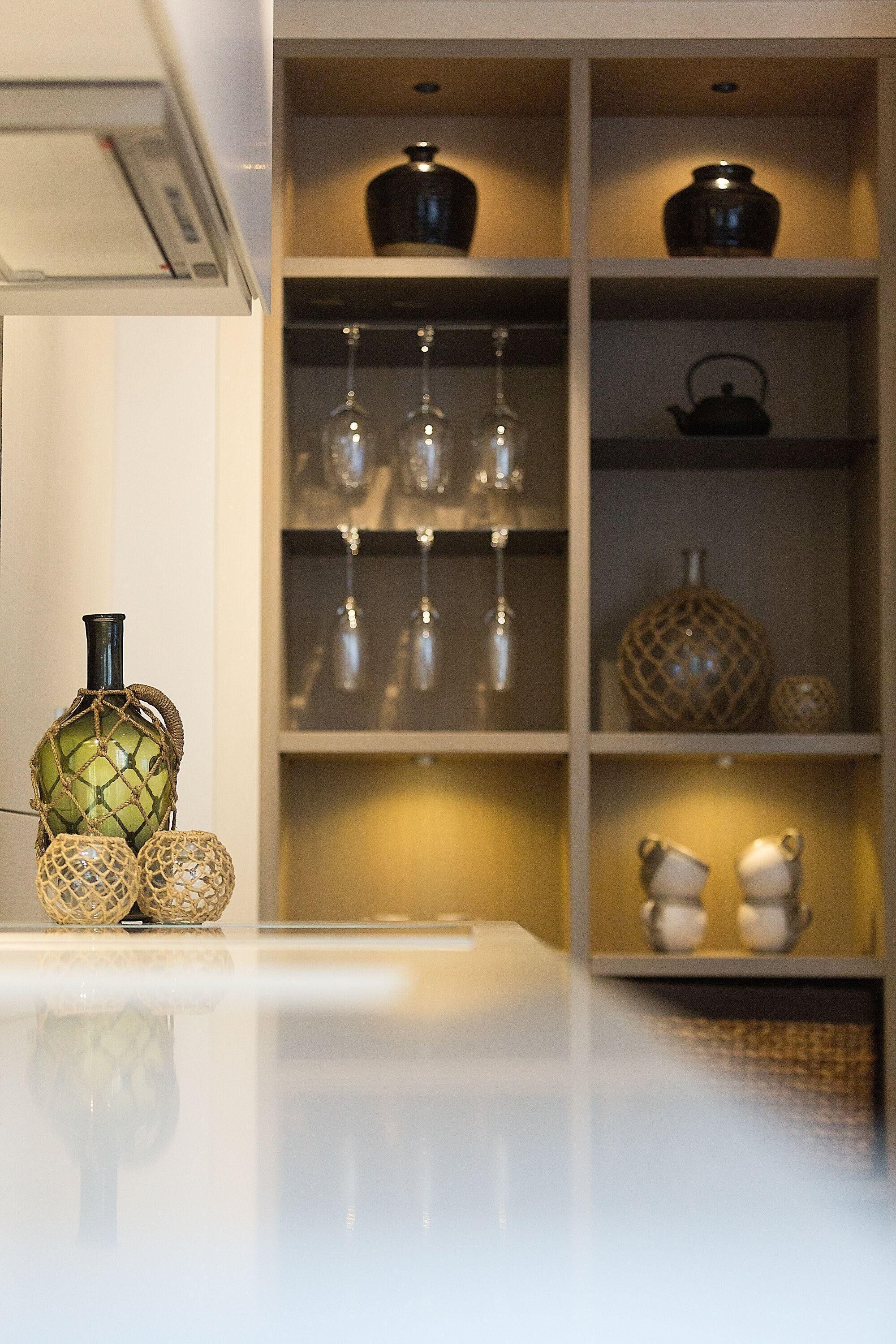 A kitchen with a white countertop, a green vase, and shelves with glassware and kitchen items.
