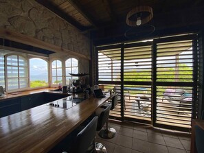 A kitchen with a large island, a view of the outdoors, and a stone wall. - Sea Lodge : Maison Avec Vue Imprenable - Votre Refuge de Vacances Idéal (Sainte-Anne)