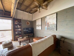 A cozy living room with a brown leather sofa, a wooden coffee table, and a bookshelf filled with books. - Sea Lodge : Maison Avec Vue Imprenable - Votre Refuge de Vacances Idéal (Sainte-Anne)