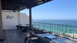 A balcony with lounge chairs, a table, and chairs, overlooking a beach. - Spend your Christmas week in Cabo at Villa La Valencia (San José del Cabo)