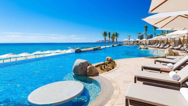 A pool area with lounge chairs and umbrellas, a clear view of the ocean, and a rocky island feature. - Spend your Christmas week in Cabo at Villa La Valencia (San José del Cabo)