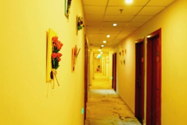 Um corredor com paredes amarelas, portas à direita e um buquê de flores vermelhas à esquerda.