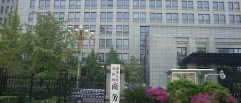 A building with a gated entrance, a sign with Chinese characters, and a flower bed with various flowers.