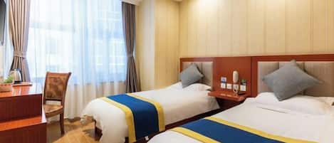 A hotel room with two beds, each with a blue and yellow bedspread, a wooden headboard, a nightstand with a lamp, and a window with curtains.