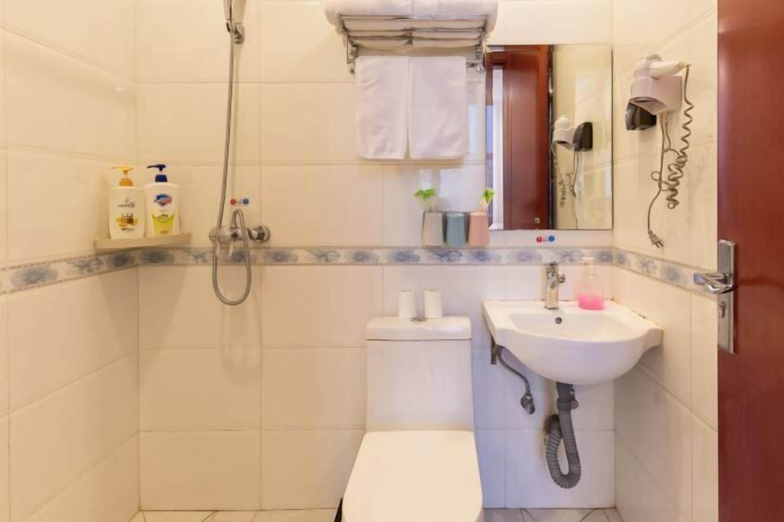 Un baño con ducha, inodoro, lavamanos y un espejo con secador de pelo.