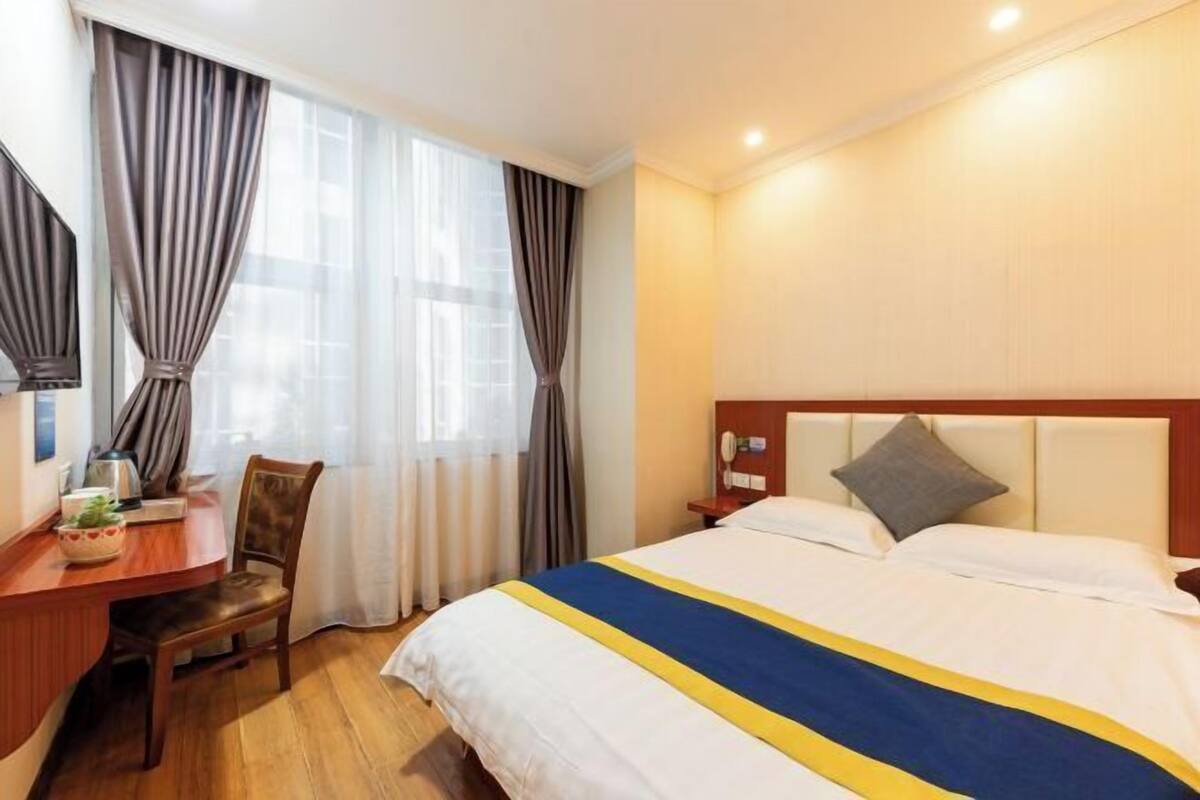A hotel room with a bed, a desk, a chair, a nightstand, and curtains.
