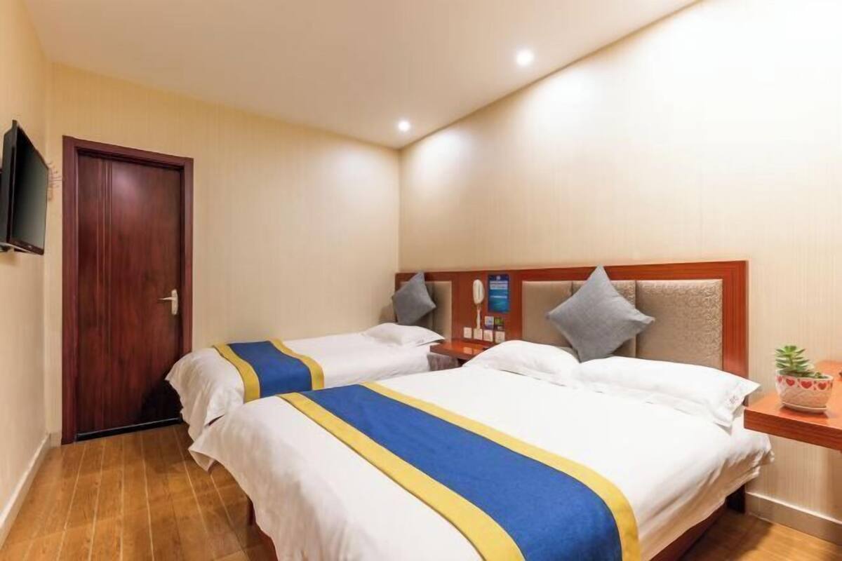 A hotel room with two beds, a wooden headboard, a small bedside table, a TV mounted on the wall, and a door.