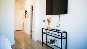 A modern living room with a flat-screen TV mounted on the wall, a glass console table with decorative items, and a wooden floor.