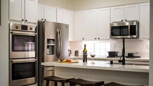 A modern kitchen with white cabinets, stainless steel appliances, a wine glass, and a bottle on the counter.