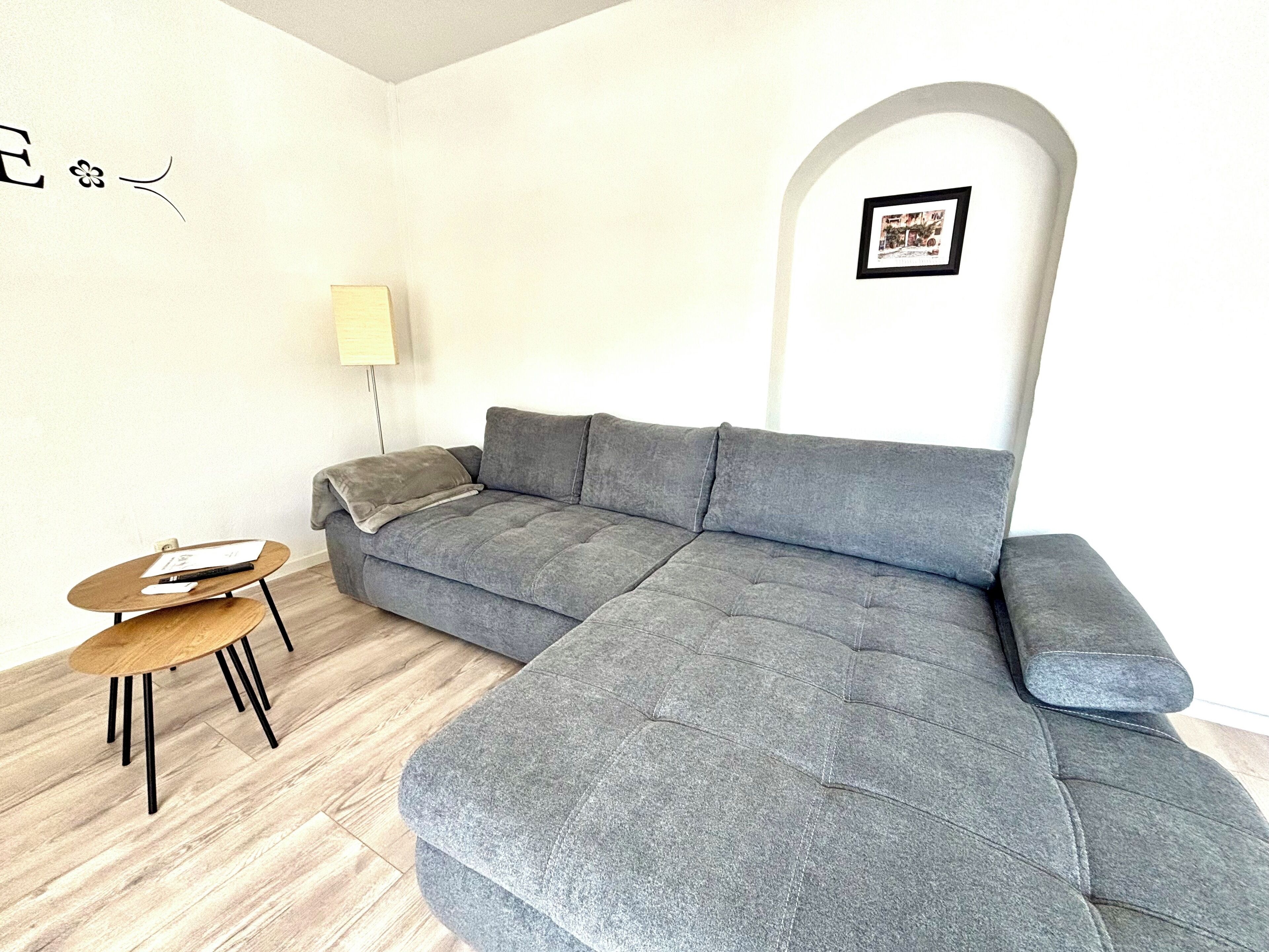 En moderne stue med en grå hjørnesofa, et lille træbord og en lampe.