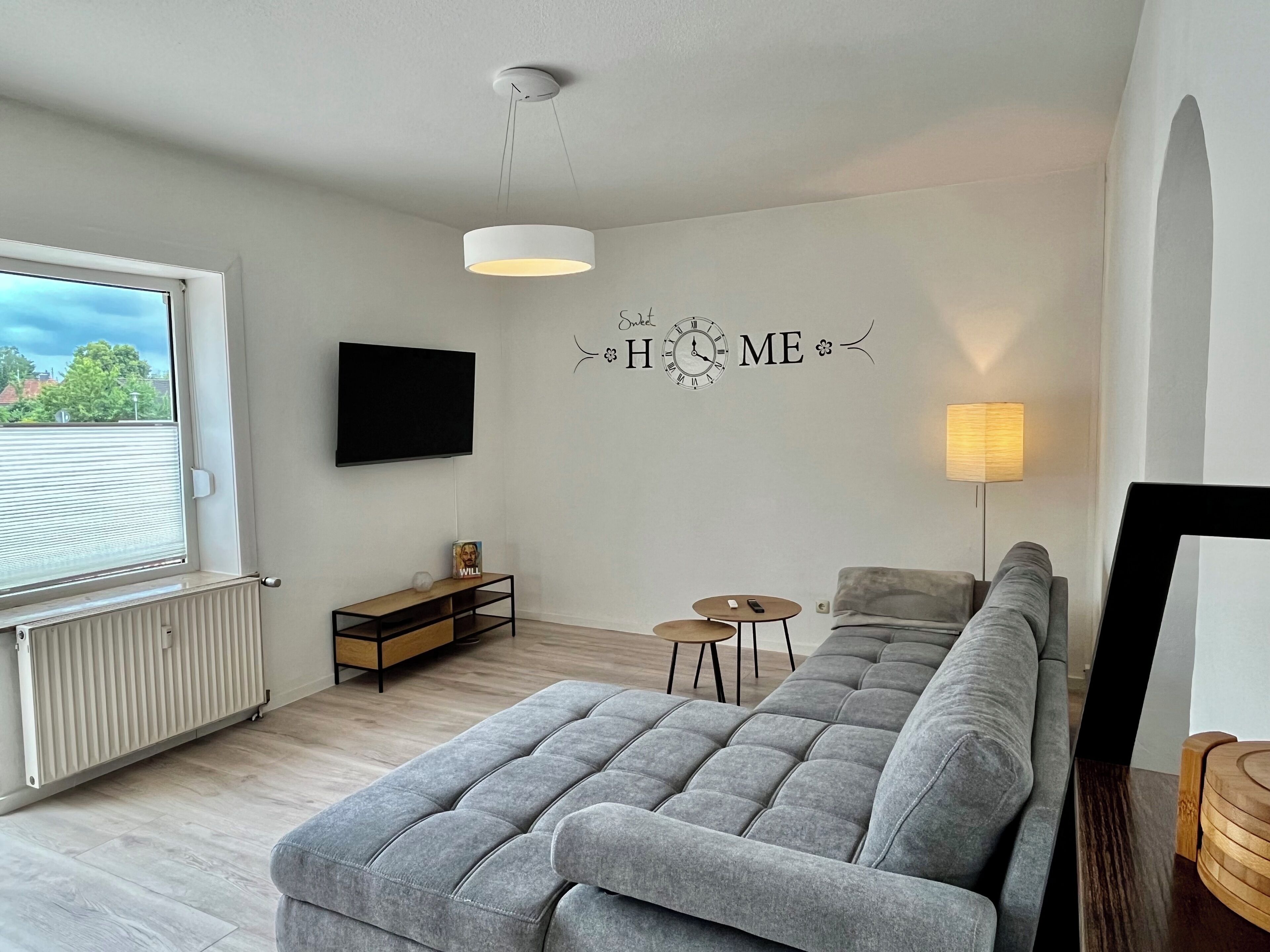 Un salon moderne avec un canapé gris, un téléviseur, une petite table et une lampe.