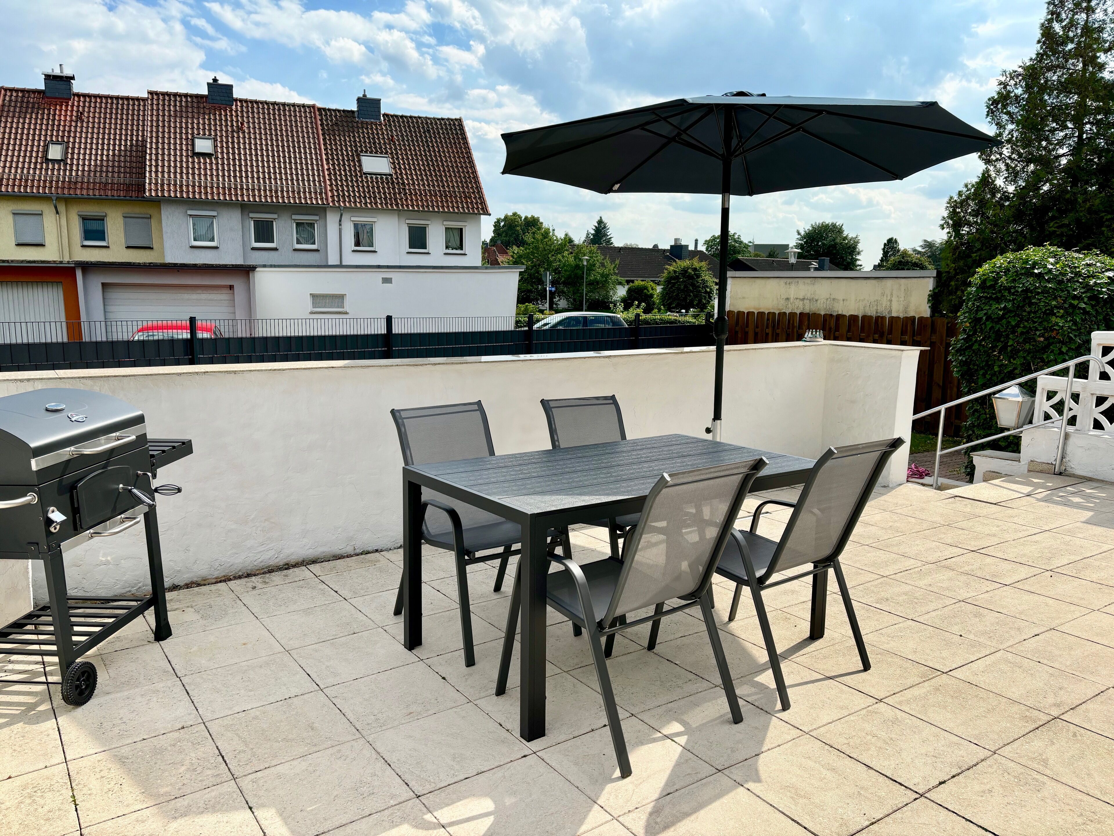 An outdoor patio with a grill, table, chairs, and an umbrella.