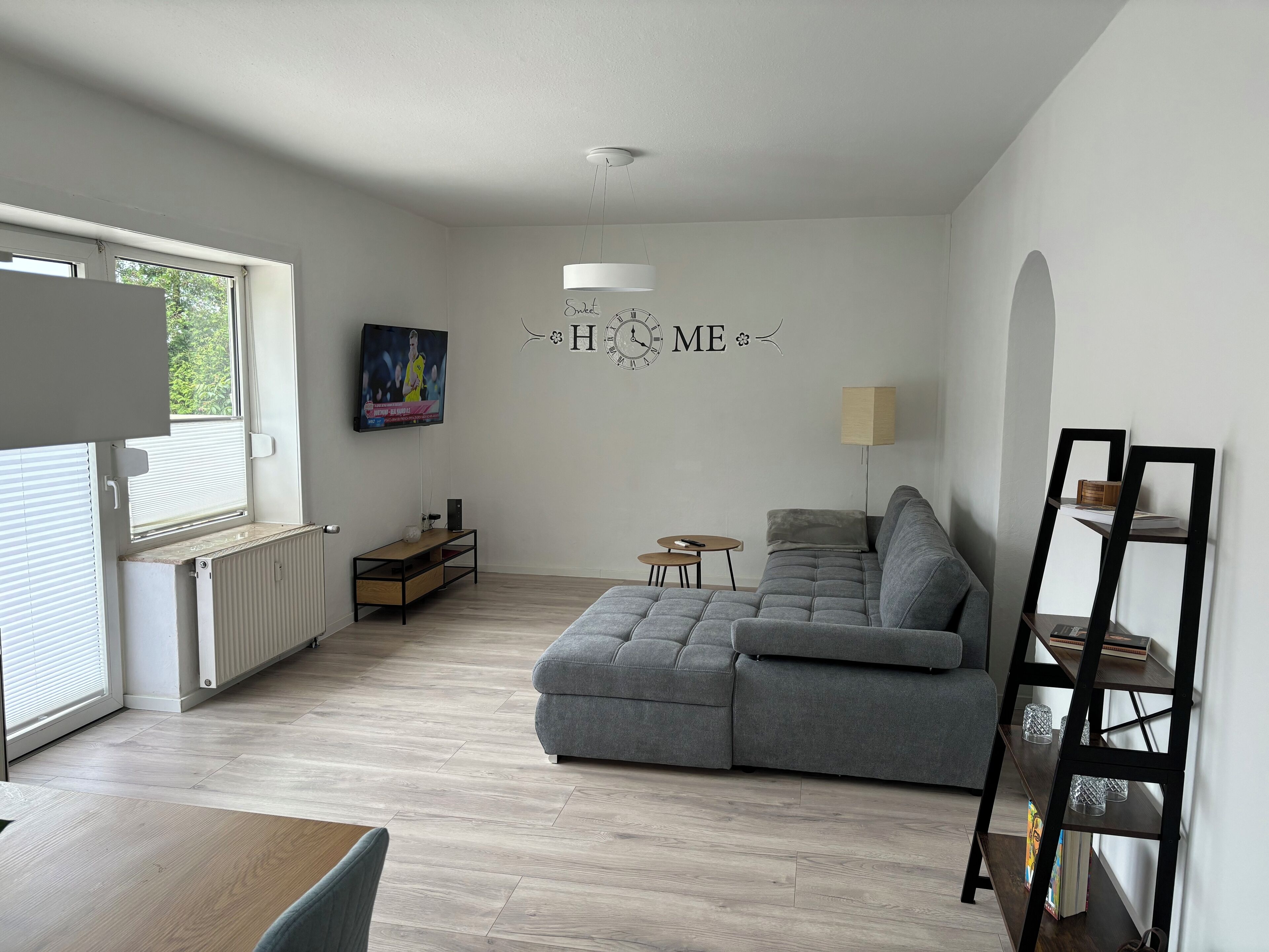 A modern living room with a grey sofa, a TV mounted on the wall, a small table, and a radiator.