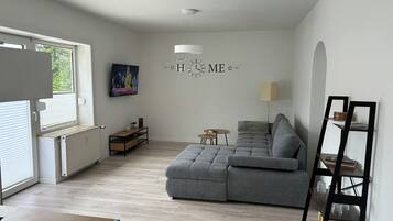 A modern living room with a grey sofa, a TV mounted on the wall, a small table, and a radiator.