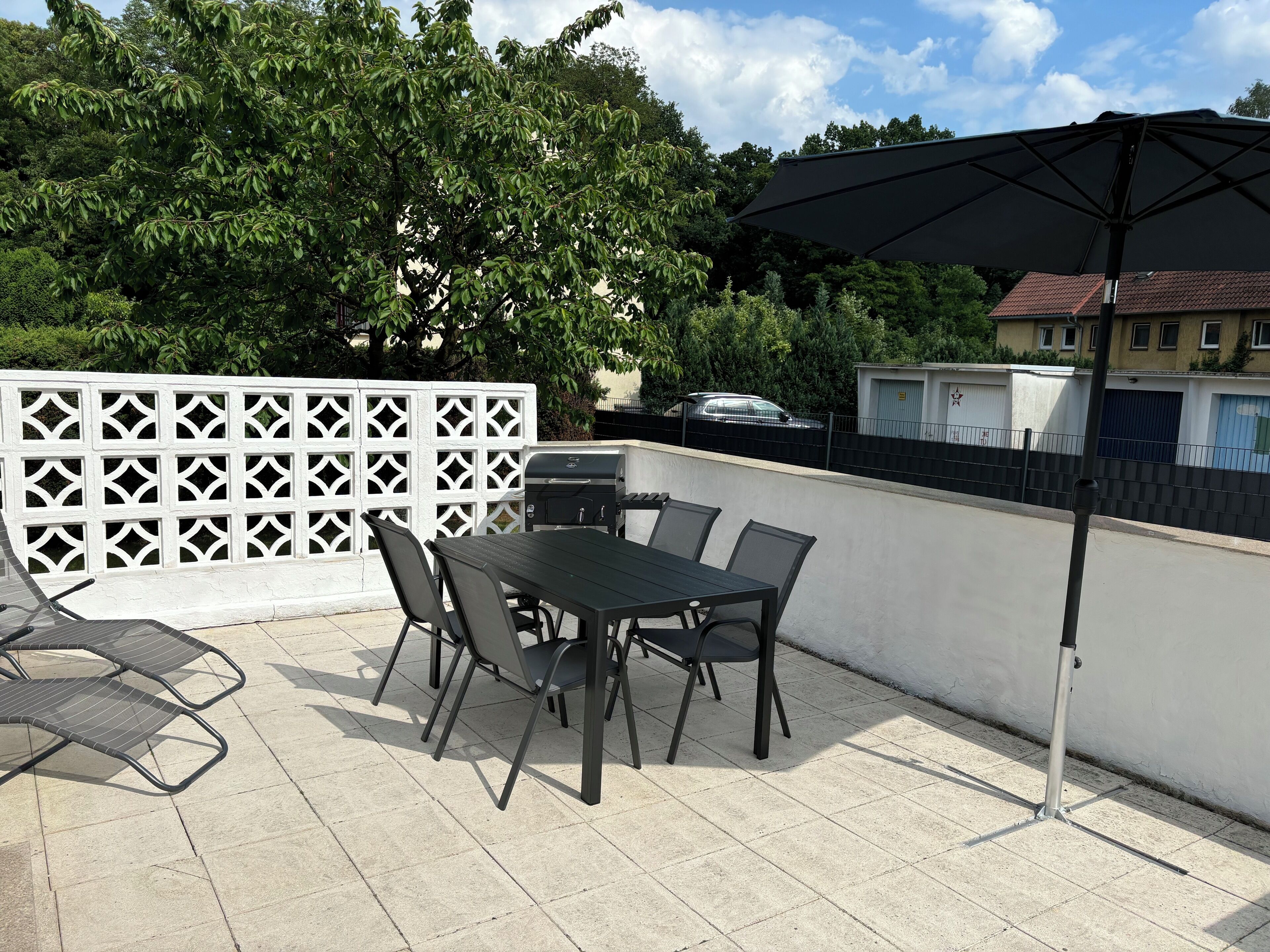 An outdoor patio with a table and chairs, a grill, and a white lattice fence.
