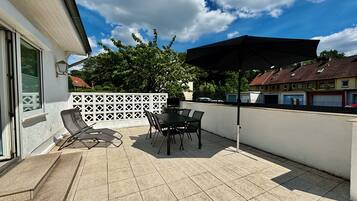Eine Terrasse mit Tisch, Stühlen, einem schwarzen Sonnenschirm und einem weißen Zaun.