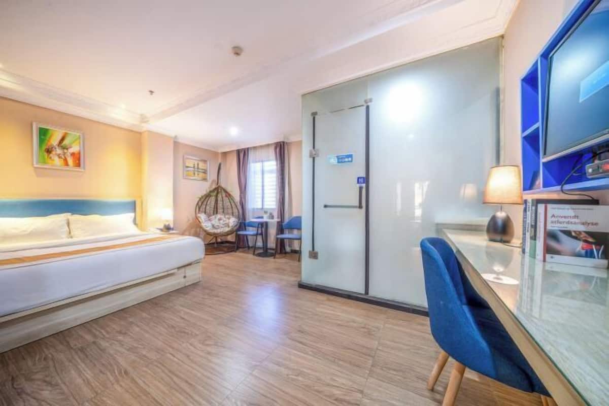 A hotel room with a bed, a desk, a chair, a glass partition, and a television.